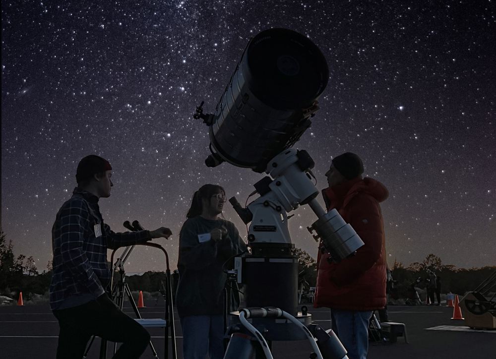A silhouetted figure at a telescope under the stars